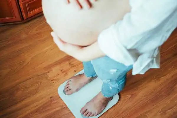 Image of woman weighing herself and experiencing weight gain through pregnancy Tilehurst